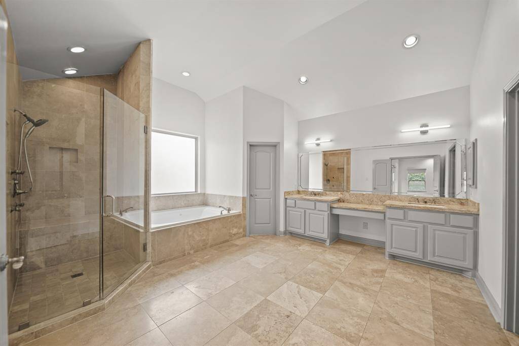 The Spa-like Primary Bath (Approximately 16'5" x 14'3") offers a Raised Trey Ceiling, Fresh Designer Paint, Travertine Tile Floors, Recessed Lighting, and Private Water Closet with Kohler Commode and Rain Glass Window.