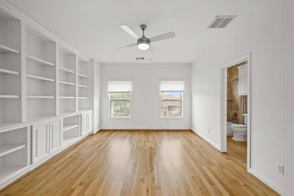 The Gameroom offers Brand New (April 2025) Refinished Natural Hardwood Floors, Ceiling Fan, Floor Mounted Electrical Outlets, Fresh Designer Paint, and Wall to Wall Built in Shelves with Cabinets below.  Two Sets of Windows view the Grassy Side Yard and provide Soft, Natural Light.
