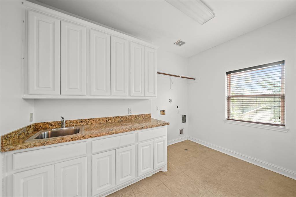 The Second Floor Laundry Room offers a Granite Topped Folding Counter with White Painted Cabinets and Drawers below, Stainless Steel Sink and Polished Chrome Faucet, White Painted Built in Cabinets, Wall Mounted Shelf with Drying Rod, and Fresh Designer Paint.  A Full Size Admiral Washing Machine and Dryer Remain (per Seller).  Additional Amenities include Fluorescent Light, Wood Stained Faux Wood Blinds, Travertine Style Floors, and Electric and Gas Dryer Connections.
