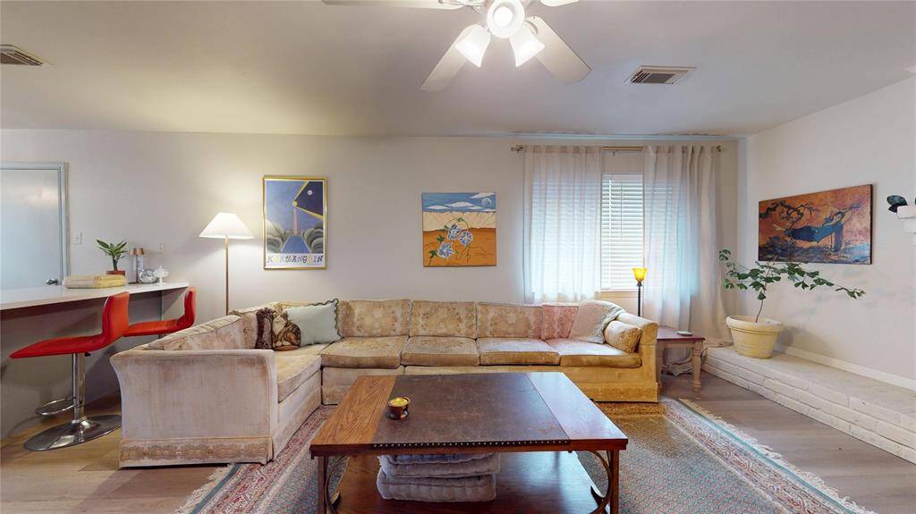 This cozy living room features a large sectional sofa, vibrant wall art, and ample natural light. It includes a ceiling fan, stylish bar seating, and a comfortable area rug, creating a welcoming atmosphere for relaxation and entertaining.