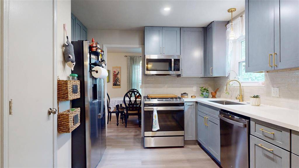 This kitchen features modern gray cabinetry, stainless steel appliances, and a sleek countertop. It has a bright and airy feel with ample natural light from the window, and provides easy access to the dining area.