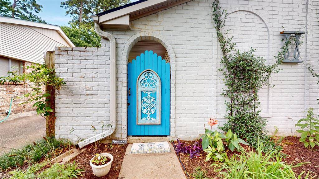 Charming entrance featuring a vibrant blue arched door set in a white brick wall. Surrounded by lush greenery and colorful plants, offering a welcoming and unique curb appeal.