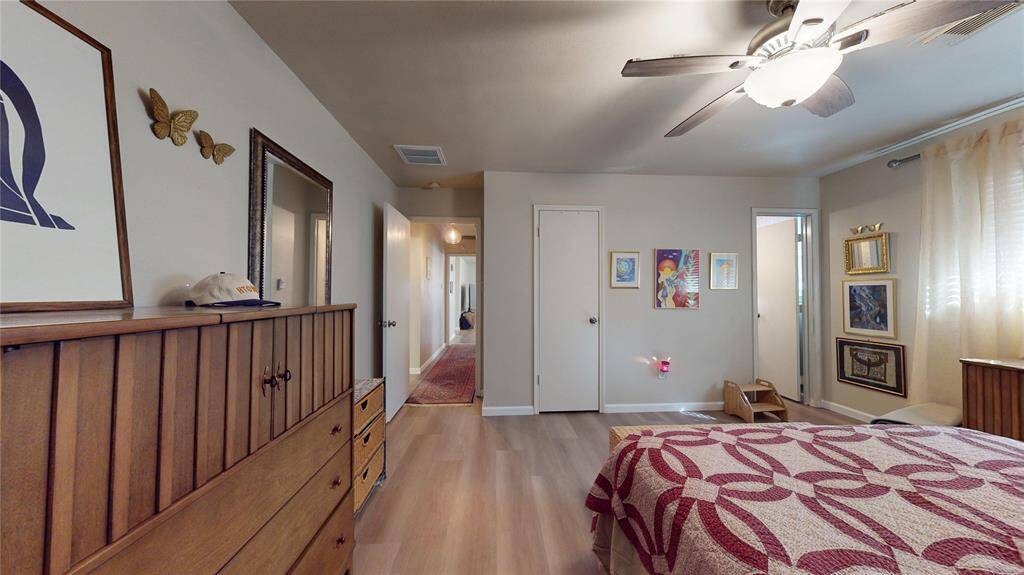 This inviting primary bedroom boasts hardwood floors, a ceiling fan, and soft neutral walls. Enjoy abundant natural light through sheer curtains, complemented by elegant wall art and a stylish wooden dresser. A convenient hallway connects to the rest of the home.