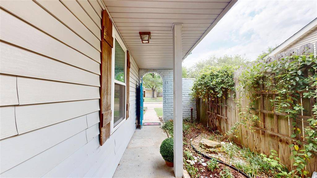 This photo displays a cozy side pathway with light-color siding and a large window, leading to an open front yard. The path is bordered by a wooden fence adorned with lush greenery, offering a welcoming and private entrance.