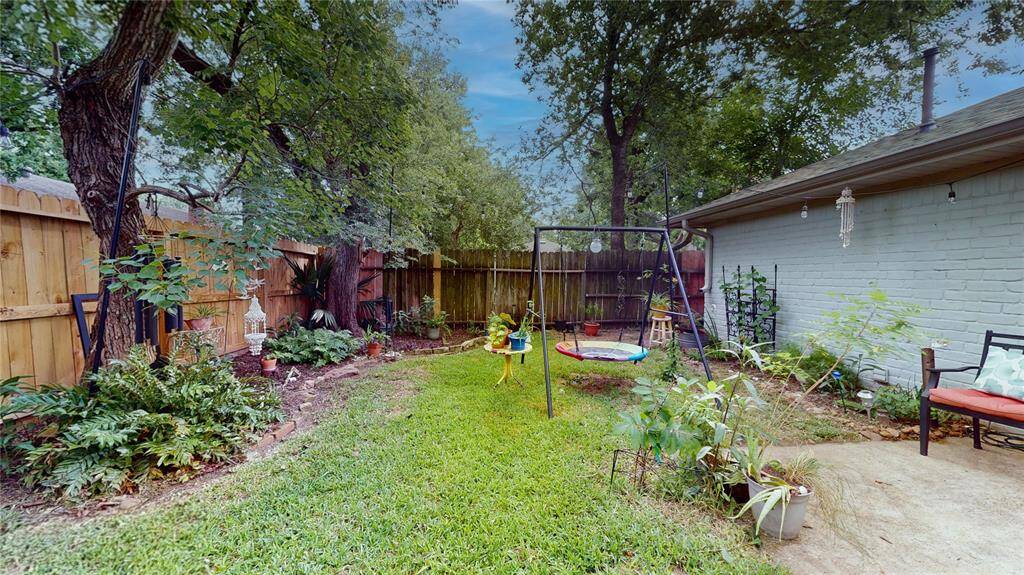 Charming backyard with a mix of grass and patio space, featuring a swing set and mature trees for shade. Ideal for relaxation and family activities.