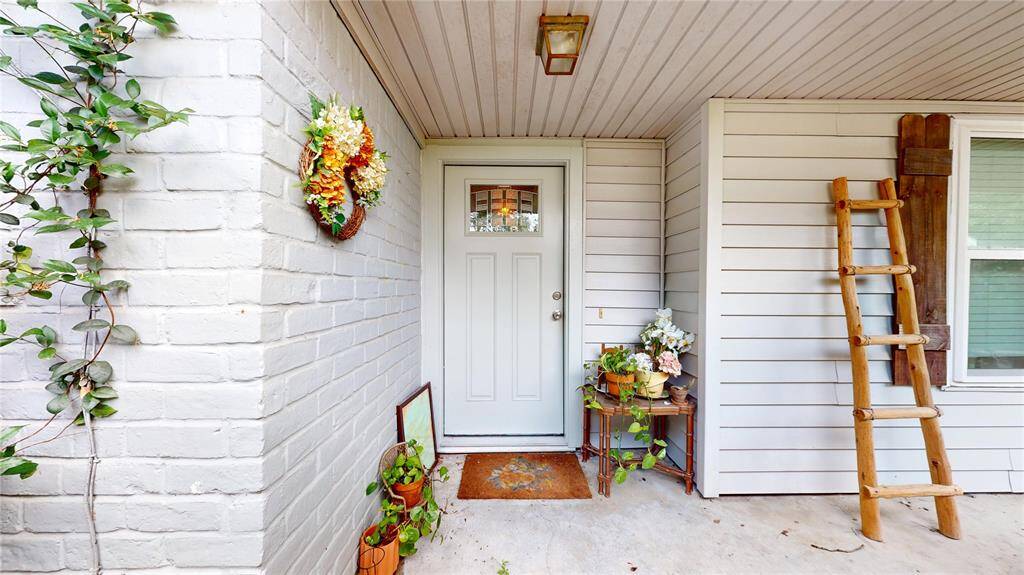 Charming entryway with a white door, surrounded by brick and siding. Decorated with plants, a ladder, and a floral wreath, creating a welcoming atmosphere.