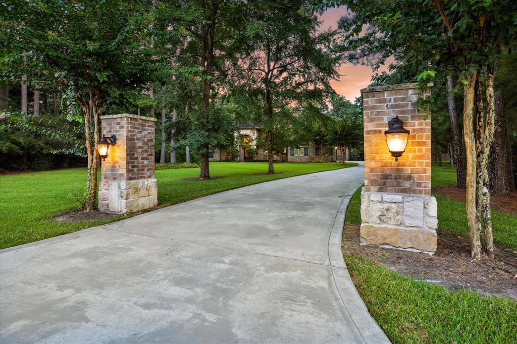 A stately, tree-lined drive welcomes you through brick and stone columns with lantern-style lighting, setting the tone for the elegance that awaits. The long private driveway gently curves through beautifully manicured grounds, offering a grand sense of arrival as it leads to the impressive façade of 10250 Clubhouse Circle.