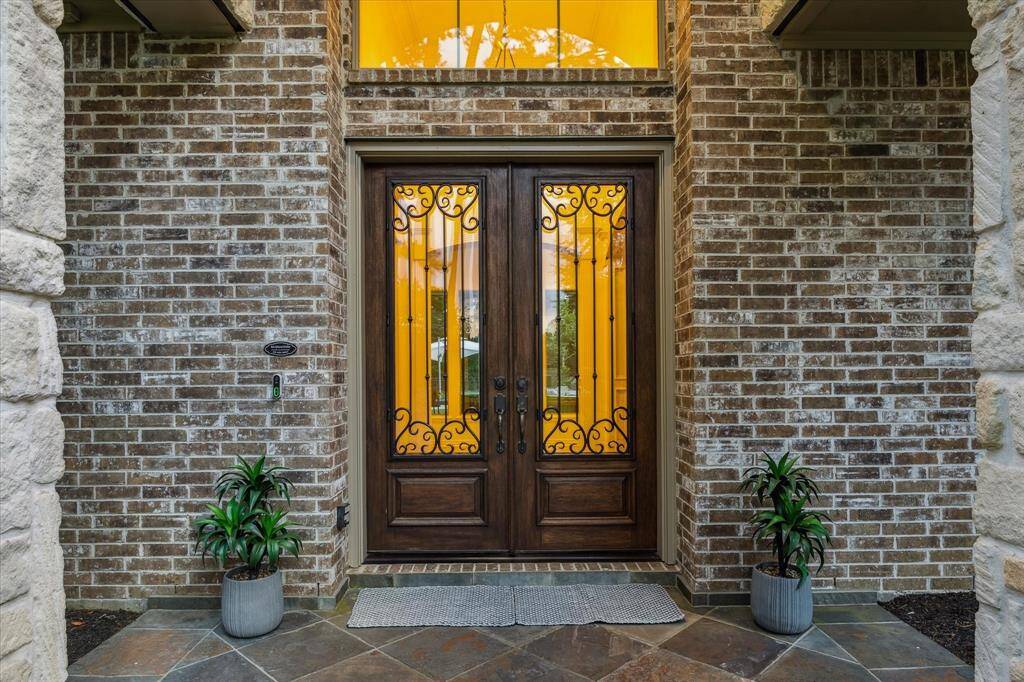 A pair of custom double doors with decorative wrought iron accents welcomes you into the home, framed by stonework and warm uplighting. This inviting entrance sets a refined tone and hints at the craftsmanship found throughout the interior.