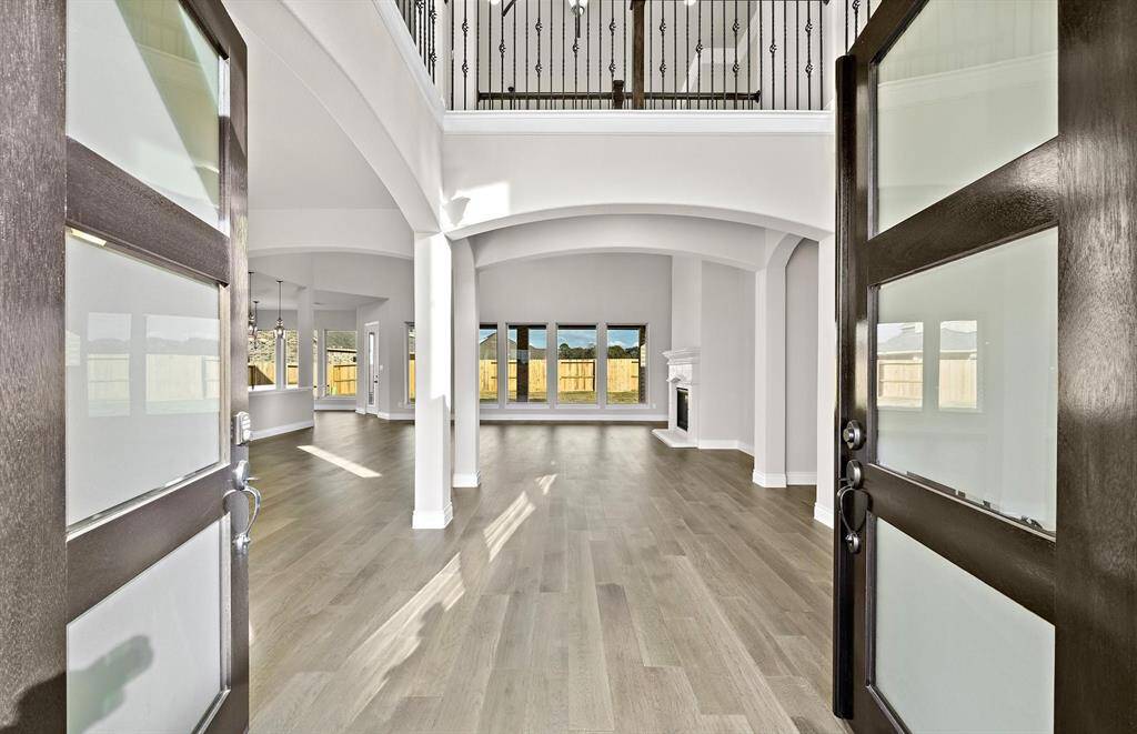 Stunning two-story entryway featuring 21-foot ceilings and natural light pours in through soaring windows, showcasing the warm wood floors that flow seamlessly throughout the main living spaces.