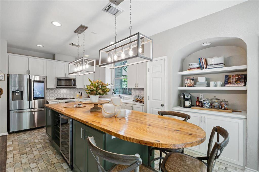 This alternate view of the kitchen highlights the built-in coffee bar and arched display nook, adding both charm and functionality. A spacious island anchors the space, while modern lighting and stainless steel appliances complete the sleek, inviting design.