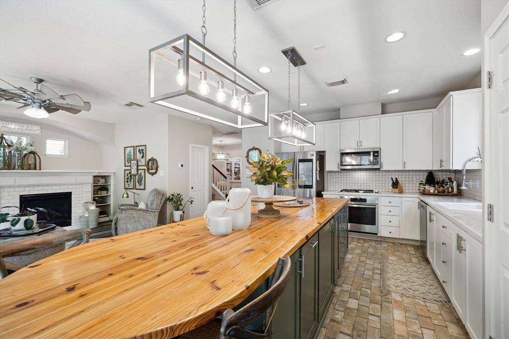 This alternate kitchen view showcases the seamless connection to the living area and entryway, enhancing the open-concept feel. The warm butcher block island takes center stage, framed by sleek lighting, white cabinetry, and a modern backsplash that ties it all together.