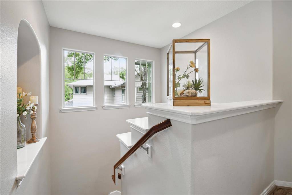 A bright and airy stair landing is illuminated by a trio of tall windows, bringing in natural light and outdoor views. The clean lines, soft wall tones, and thoughtful decorative niche create an elegant transition between floors.