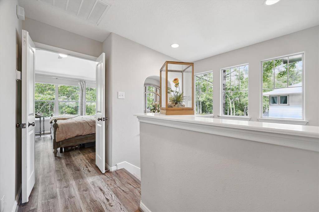 This additional view of the upstairs landing offers a bright transition space framed by large windows and natural light, leading gracefully into the serene primary suite. Warm flooring and soft wall tones add to the airy, cohesive flow.