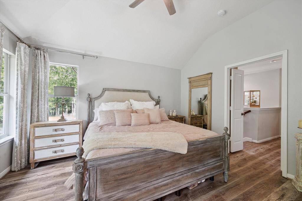 This alternate view of the primary bedroom highlights its airy layout and serene connection to the upstairs landing. Large windows frame lush greenbelt views, while soft tones and rustic wood textures create a calming, retreat-like atmosphere.