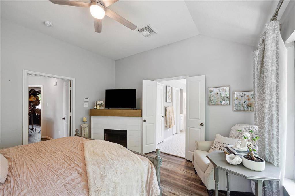 This alternate view of the primary bedroom offers a cozy look toward the ensuite bath, complete with a charming corner sitting area for added ambiance. Soft tones and layered textures create a calming atmosphere with seamless flow into the spa-like bath beyond.
