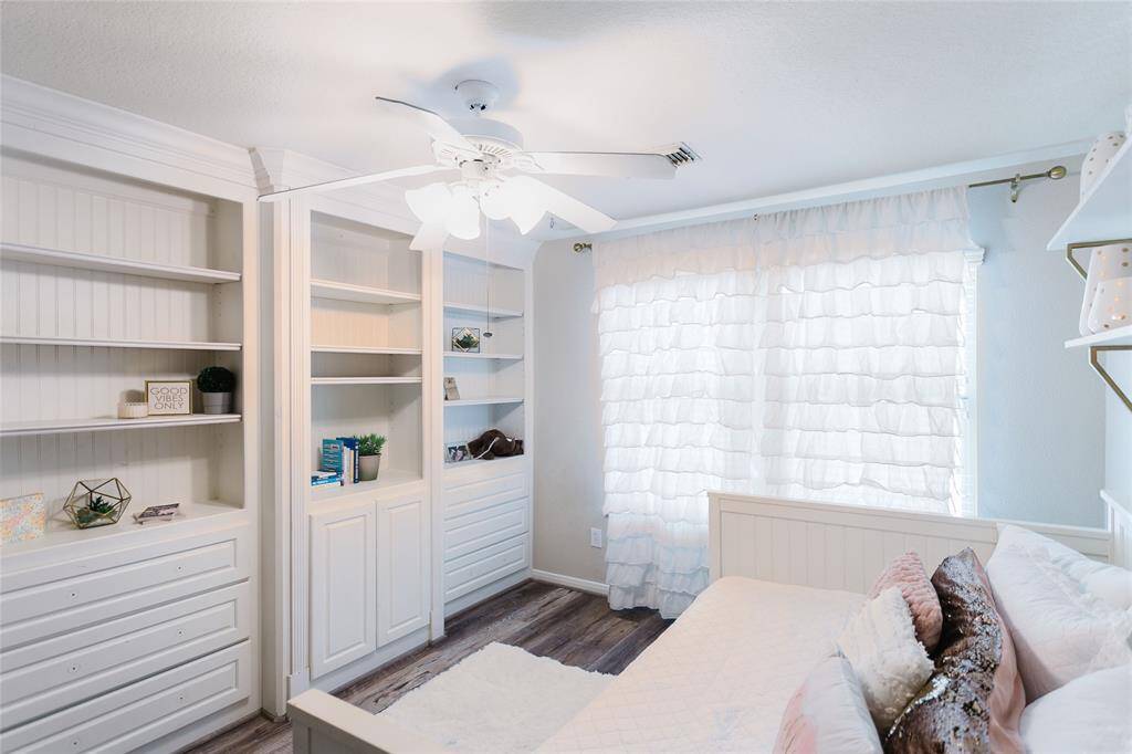 This alternate view showcases the custom built-in cabinetry and shelving that add both charm and practical storage to the secondary bedroom. Thoughtful styling, natural light, and soft textures enhance the cozy, cheerful feel—making it a delightful space for rest, play, or study.