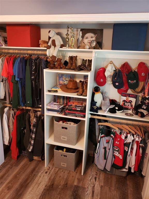 This well-styled closet offers a great example of how to organize a secondary bedroom for both function and personality. Open shelving showcases favorite items, books, and trophies, while dual hanging rods and labeled bins maximize storage. Sports gear and accessories are neatly displayed, creating a space that’s as practical as it is personal.