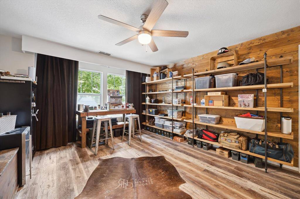 This versatile upstairs game room blends rustic charm with practical functionality. The warm wood accent wall creates a great backdrop for open, portable shelving—ideal for organizing hobbies, collections, or gear. Spacious enough to add a workbench or a cozy couch, this flexible area is perfect for crafting, gaming, or relaxing. Durable vinyl plank flooring and abundant natural light complete the inviting setup.