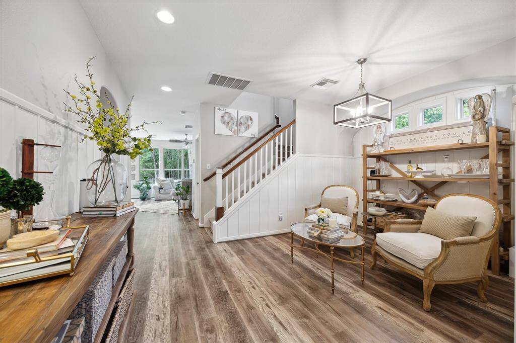 This inviting dining lounge area combines classic charm with modern style, highlighted by rich vinyl plank flooring, custom wainscoting, and transom windows that flood the space with natural light. A contemporary chandelier adds a polished touch, and the thoughtfully curated furnishings make this a perfect spot for intimate gatherings or quiet moments of relaxation.
