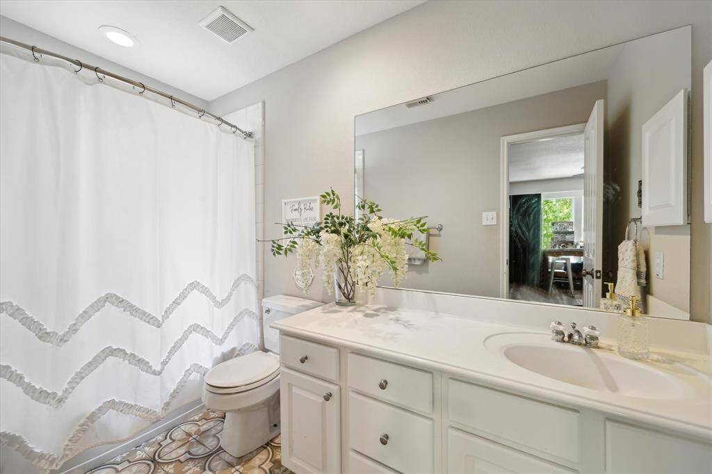 This guest bathroom is conveniently located between the secondary bedrooms, offering easy access and a fresh, inviting feel. Stylish tile flooring, a large mirror, and crisp white cabinetry create a clean and timeless look, while soft accents add a touch of charm.