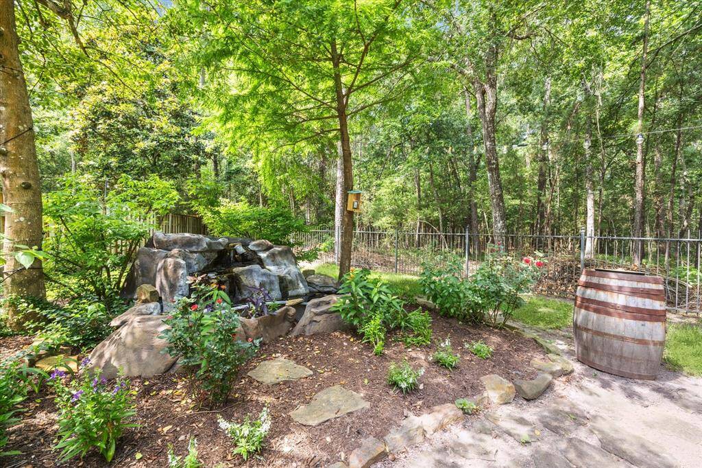 The serene rock waterfall fountain provides the soothing sounds of gently flowing water, enhancing the peaceful, nature-inspired ambiance of the backyard. Surrounded by blooming plants, lush foliage, and the backdrop of a wooded greenbelt, it creates a relaxing focal point perfect for unwinding or enjoying time outdoors.
