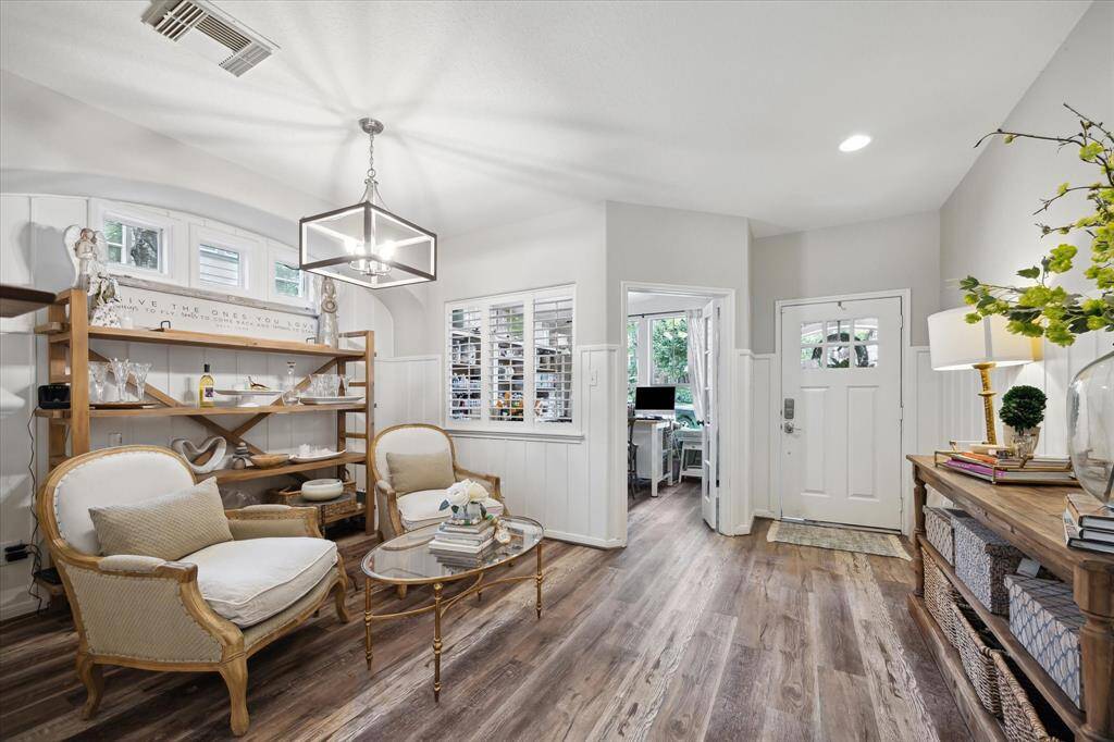 This alternate view captures the warm, welcoming flow from the entry into the flexible lounge and adjoining study or craft room. Rich vinyl plank flooring, crisp white wainscoting, and designer lighting add a sophisticated touch, while natural light from the front-facing windows enhances the inviting atmosphere throughout.