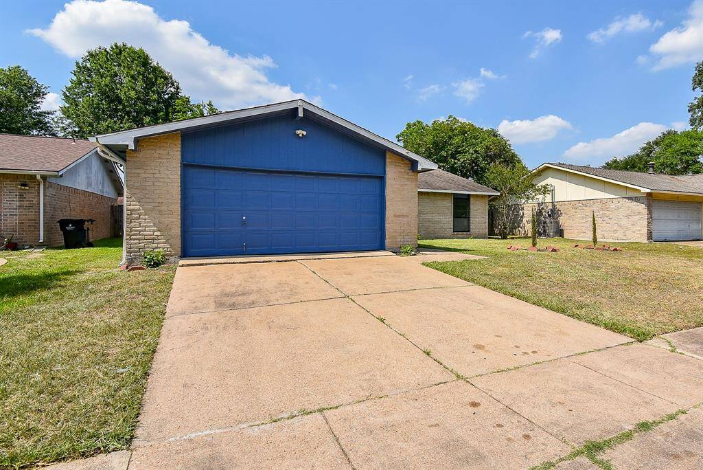 The wide garage doors are a bold pop of blue, standing out against the brick exterior. The driveway offers generous space beside the expansive lawn. The main entry is tucked away, hinting at a private welcome.