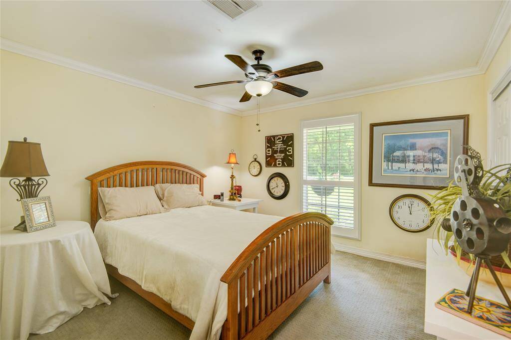 One of the three secondary bedrooms offers charming front yard views, soft pastel yellow walls, and elegant crown molding for a warm and inviting feel.