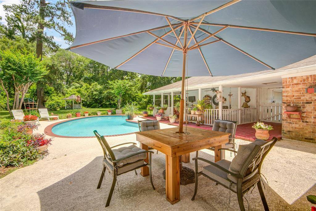 From the back patio, enjoy views of the sparkling pool ahead, lush greenery to the left and rear, and a spacious covered patio area to the right—perfect for outdoor living and entertaining.