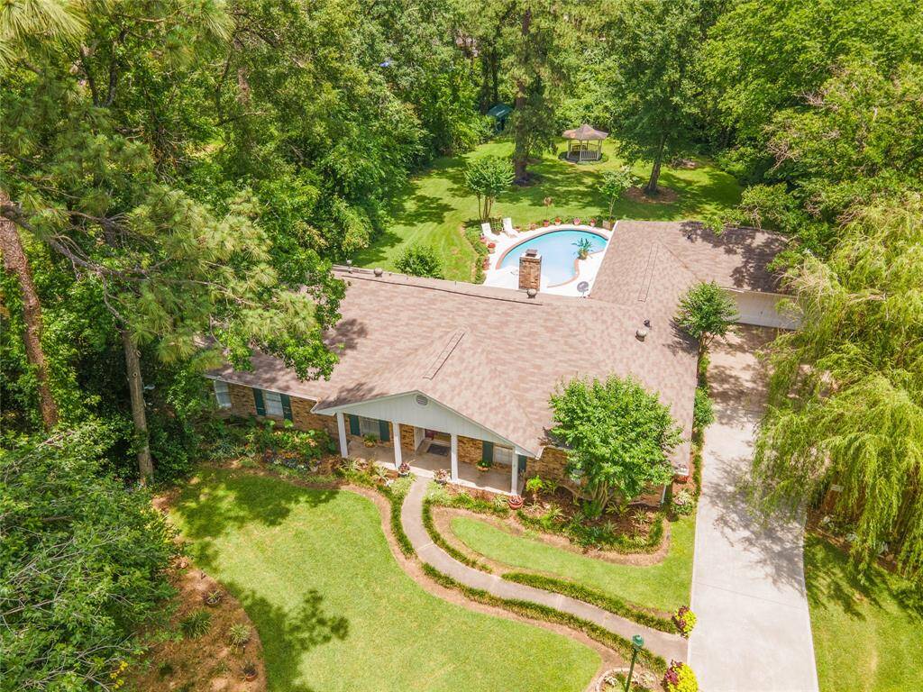 This aerial front view showcases the expansive, tree-filled lot with a glimpse of the backyard pool and gazebo nestled beyond the home.
