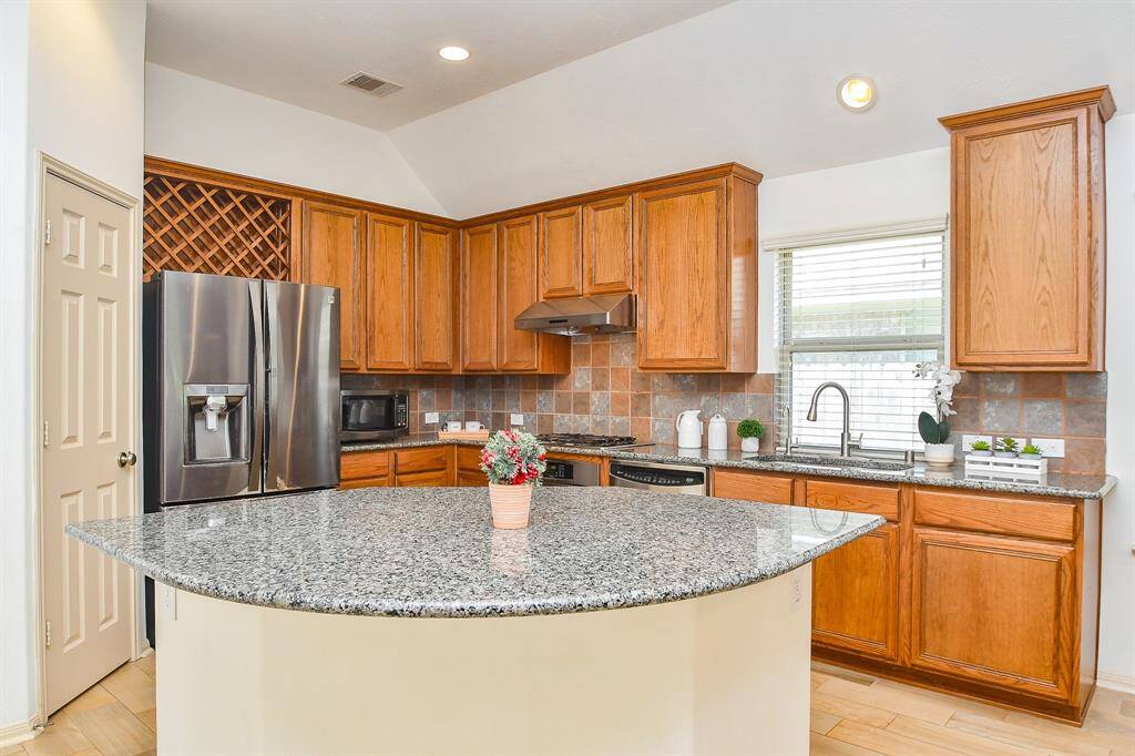 Spacious island kitchen with granite countertops, 42" cabinets, stainless steel sink, and tile backsplash.
