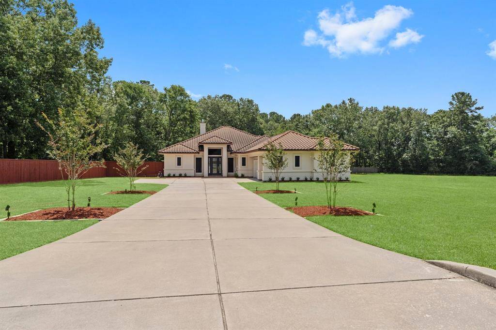 This photo showcases a modern, single-story home with a tiled roof, set back from the road by a long driveway. It features a large, well-maintained lawn and is surrounded by trees, offering a private and serene environment. The exterior is clean and inviting, with a spacious front yard.