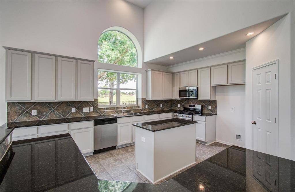 This modern kitchen features high ceilings, ample cabinetry, and sleek black countertops. A large arched window provides plenty of natural light, and stainless steel appliances add a contemporary touch.