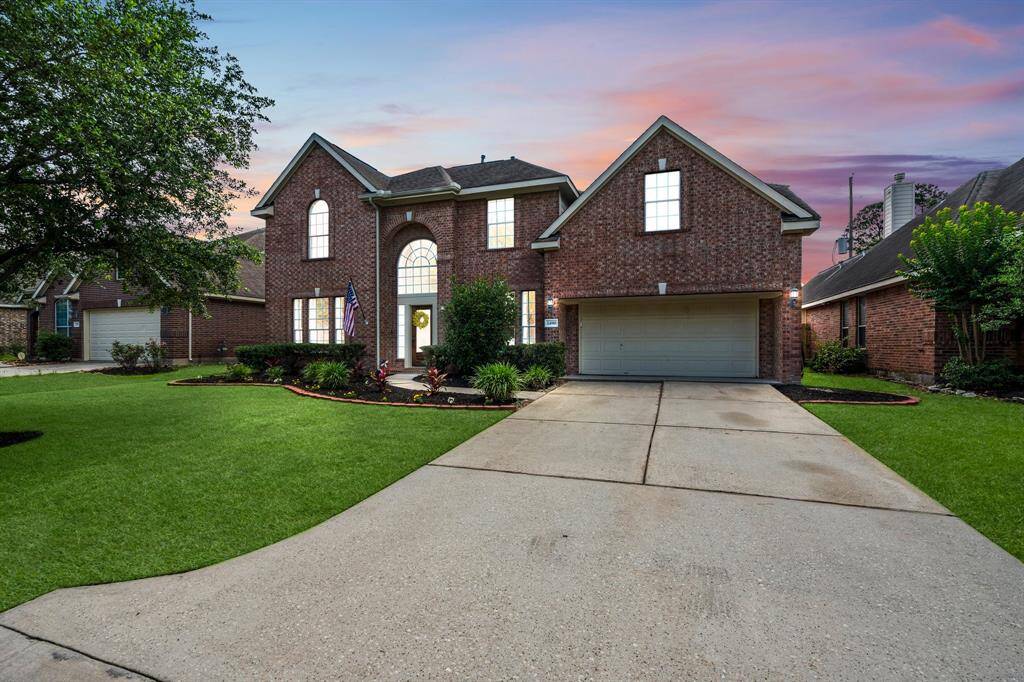 Elegant two-story brick home with arched entry, tall windows, and manicured landscaping.