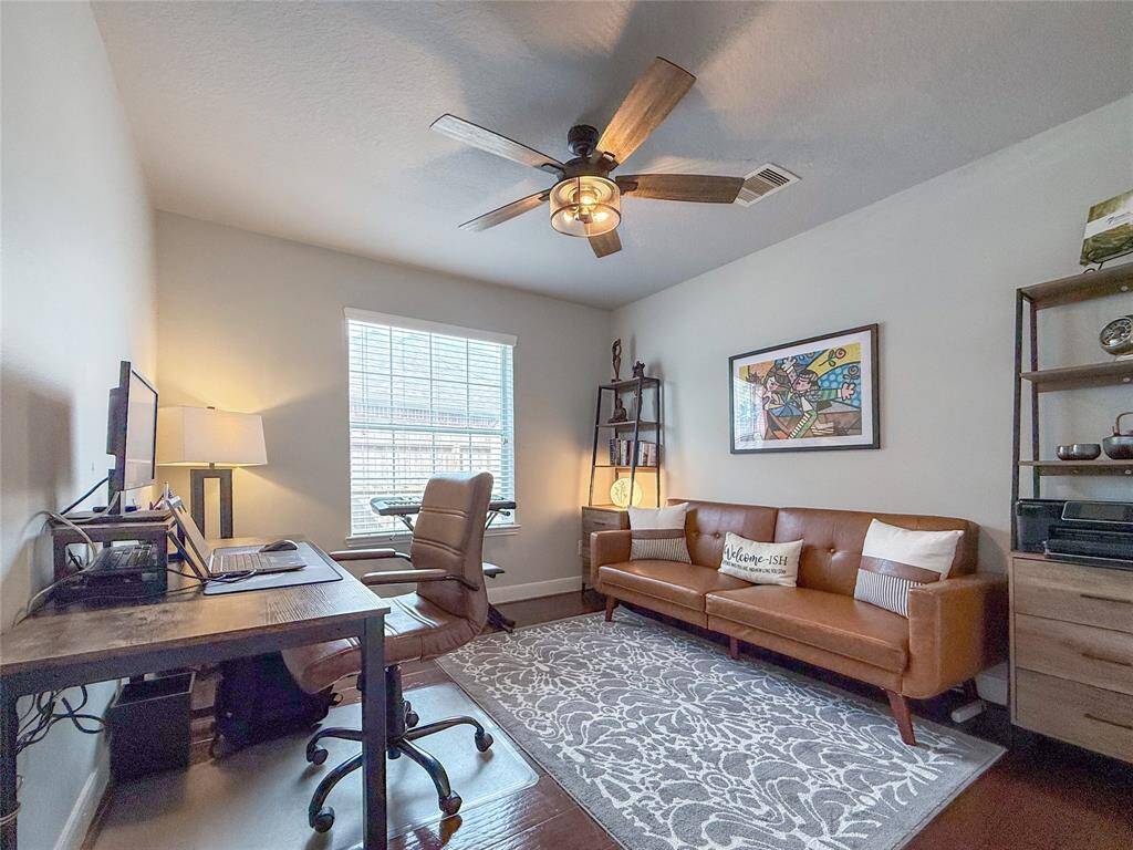 This cozy home office features a comfortable setup with a desk and chair, a stylish ceiling fan, and a window providing natural light.