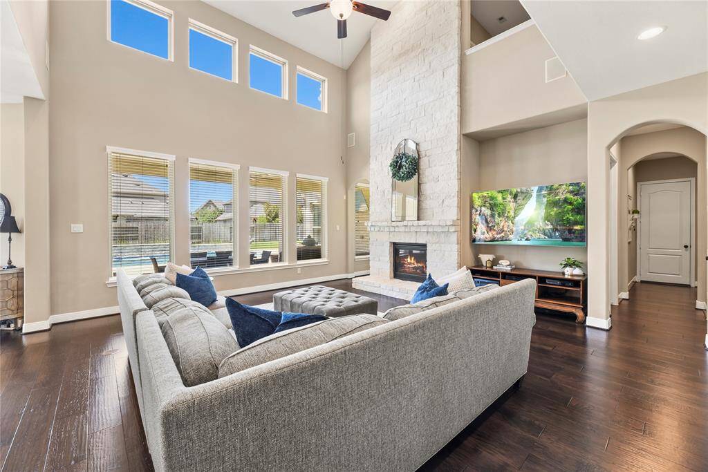 Spacious family room features high ceilings, abundant natural light from large windows, a fireplace, and elegant wood flooring.
