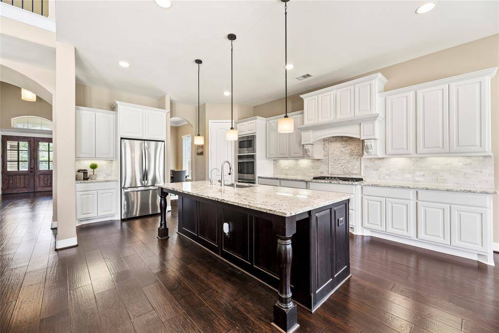 Spacious kitchen features elegant white cabinetry, a large central island with granite countertops, and stainless steel appliances including double over, microwave, and built-in range.