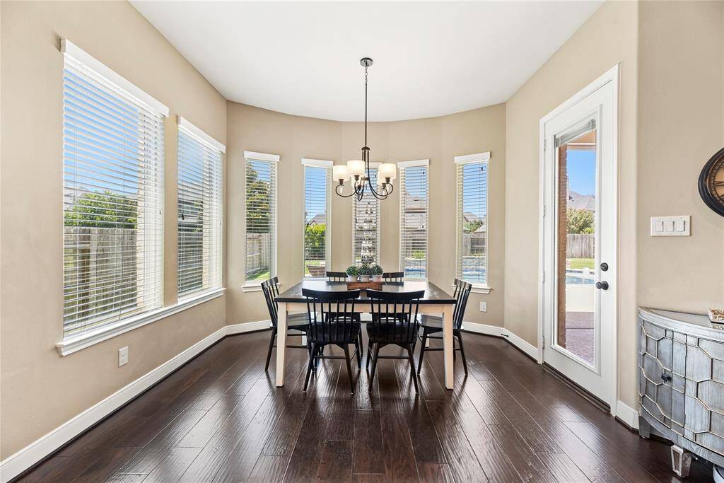 Bright breakfast nook with large windows, and hardwood floors. The room overlooks a pool and backyard, offering a serene view.