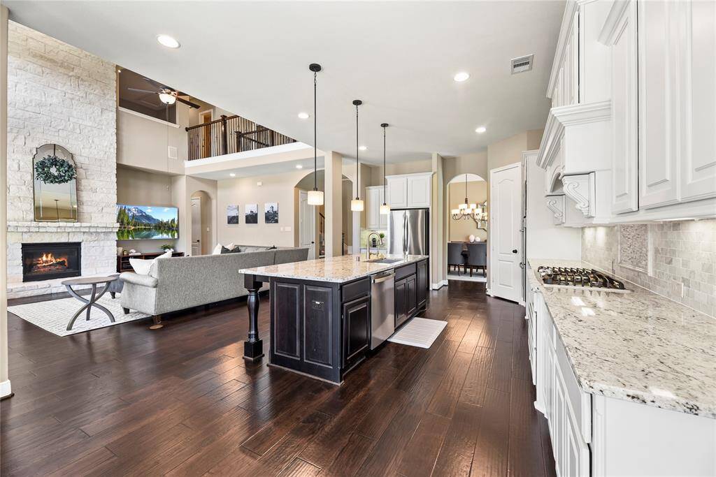 This open-concept home features a spacious kitchen with granite countertops and an island, overlooking the family room with a fireplace and high ceilings. The dining area is elegantly connected, offering a seamless flow for entertaining.