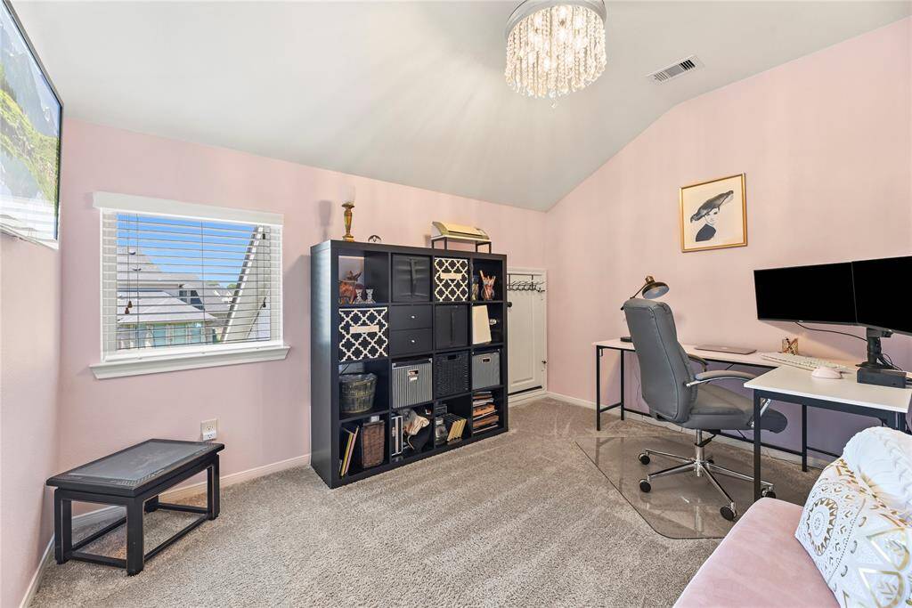 Home office features a carpet flooring and vaulted ceiling.