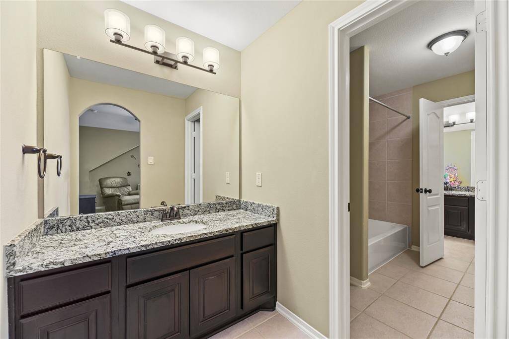 Jack-and-jill bathroom features granite countertop, a sink, vanity, and soaking tub.