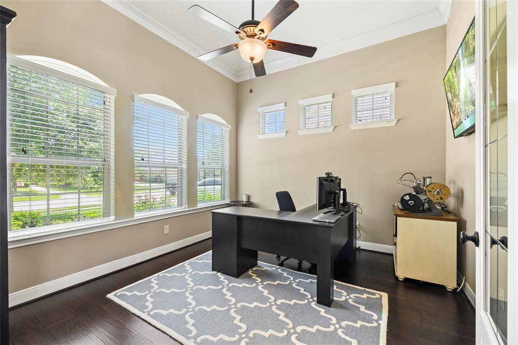 Bright home office with a ceiling fan and large windows viewing the front of the home, allowing plenty of natural light.