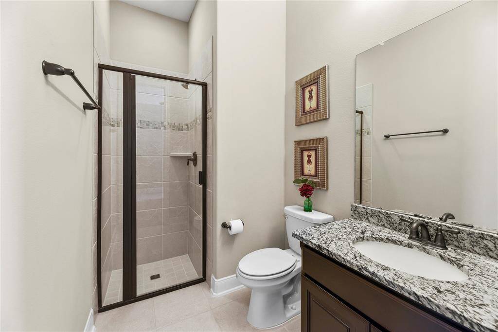 Bathroom of the first-floor bedroom features a modern design with a tiled walk-in shower, granite countertop with a sink, and vanity.