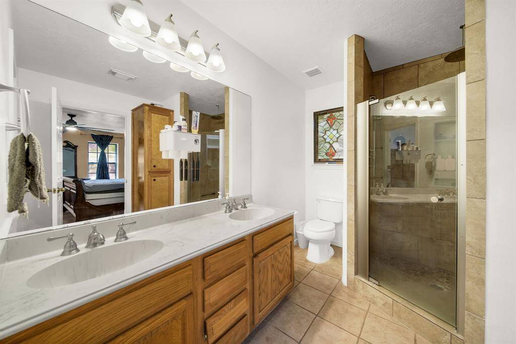 Primary bathroom boasts dual sink vanity with tiled shower.