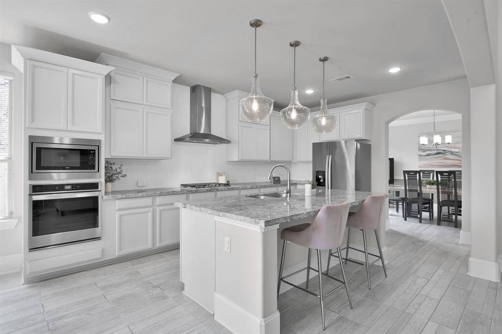 The kitchen features built-in appliances, oversized island with sink, 3 pendant lights, gas cooktop, pass through to the dining room and a nearby breakfast nook.