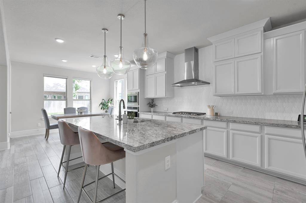 The kitchen features built-in appliances, oversized island with sink, 3 pendant lights, gas cooktop, pass through to the dining room and a nearby breakfast nook.