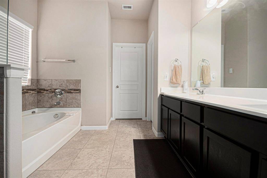 Experience luxury in the primary bathroom, featuring elegant tile floors, a spacious dual-sink vanity, and a relaxing soaking tub.
