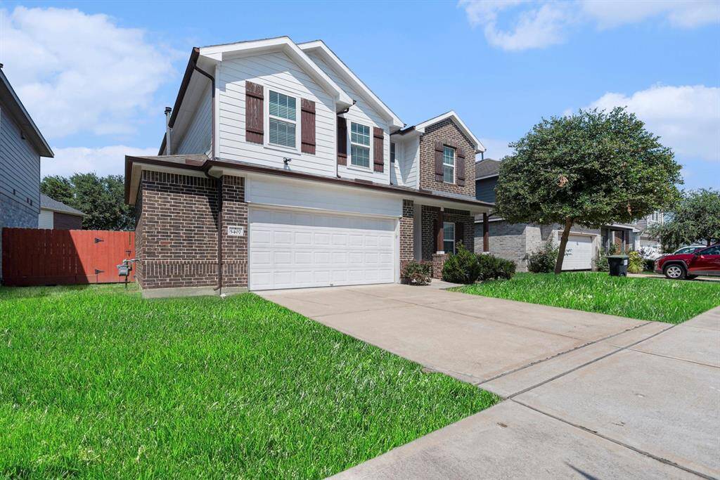 Charming two-story home with a spacious driveway, lush front lawn, and inviting brick façade.