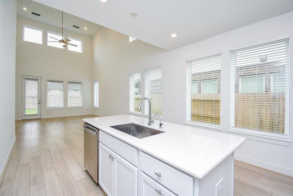 This bright, modern home features an open-concept layout with high ceilings and large windows for abundant natural light. The kitchen boasts a sleek island with a sink and stainless steel appliances, while the adjacent living area has access to a backyard patio, making it perfect for entertaining.
