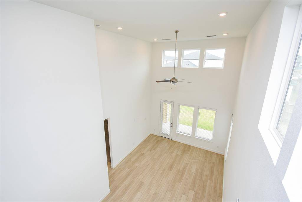 This photo showcases a spacious, bright living area with high ceilings and abundant natural light from large windows. The room features light wood flooring and a ceiling fan, creating an inviting and airy atmosphere.